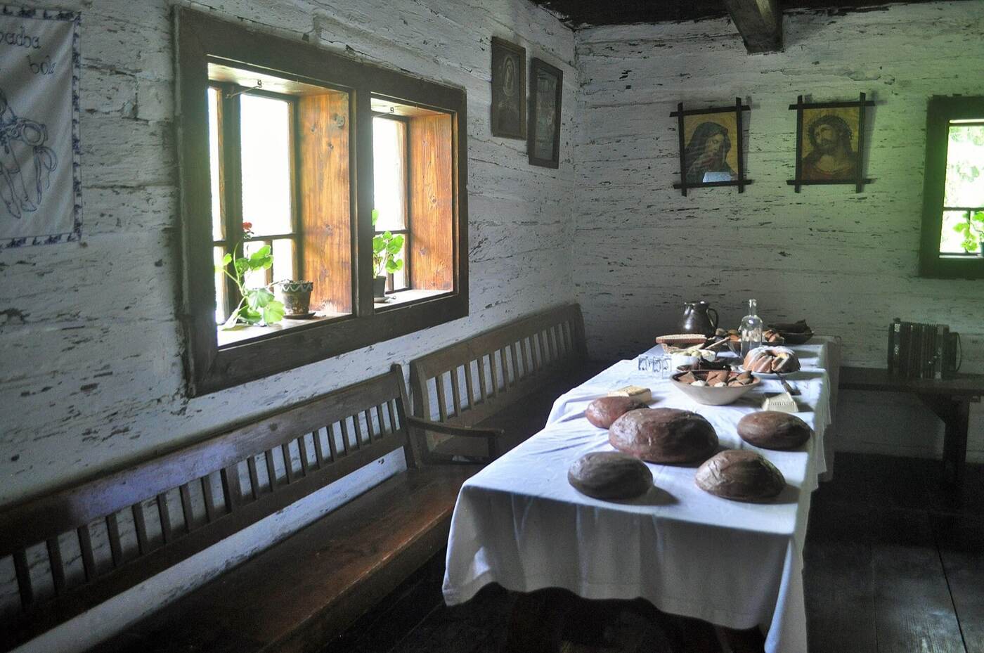A limewashed cottage kitchen with deep-set windows, a long bench, and a table laid with bread