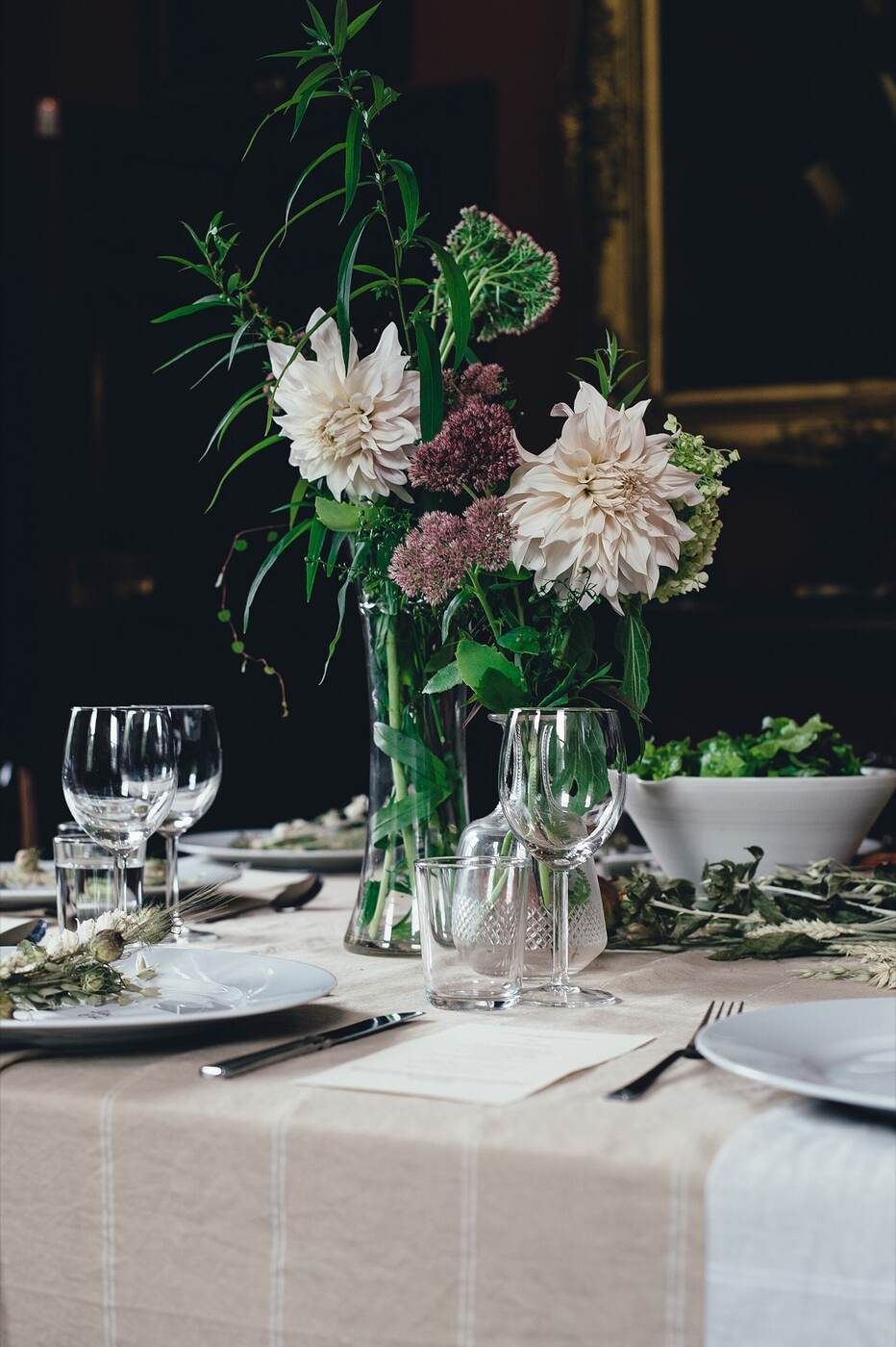 A candlelit table with garden flowers, glassware, and a striped linen runner